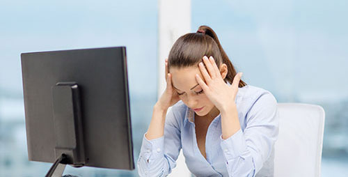 A frustrated woman in front of a computer, holding her head, highlighting the importance of reliable data backup and recovery services.